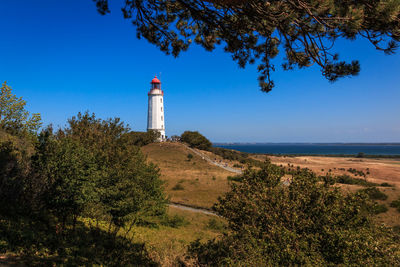 Lighthouse and trees by sea against sky