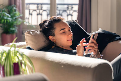 Young woman using mobile phone sitting on sofa