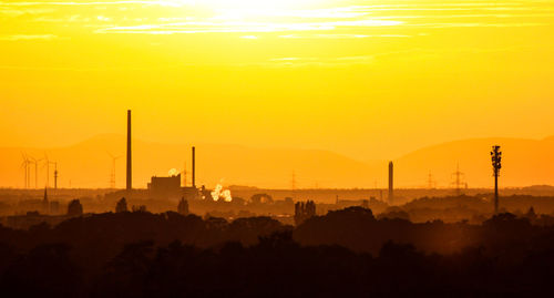 Silhouette of factory against orange sky