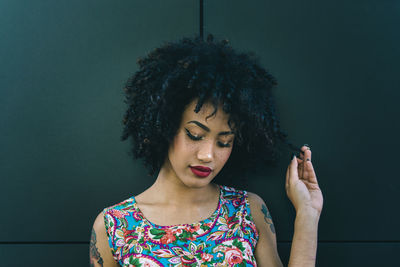 Fashionable young woman with curly hair against wall