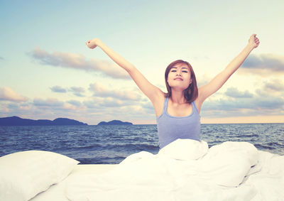 Woman stretching hands on bed against sea