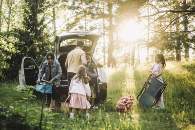 Family helping each other while unloading stuffs from car trunk in forest