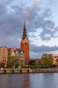 View of buildings by river against cloudy sky