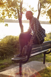 Happy man sitting on bench at park against lake