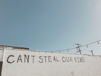 Low angle view of text on wall against clear sky