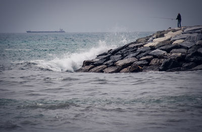 Waves splashing on rocks at shore against clear sky