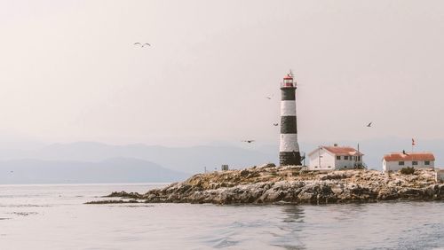 Lighthouse by sea and buildings against sky