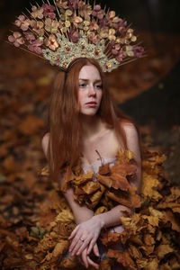 Thoughtful young female model covered with autumn leaves in forest