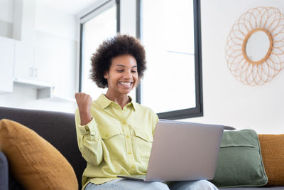 Young woman using laptop while sitting on sofa at home