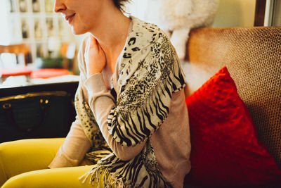 Midsection of smiling woman sitting on sofa at coffee shop