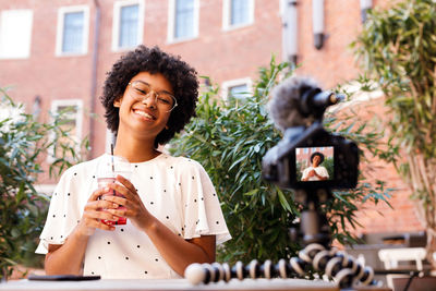 Portrait of smiling woman filming herself while having coffee in cafe