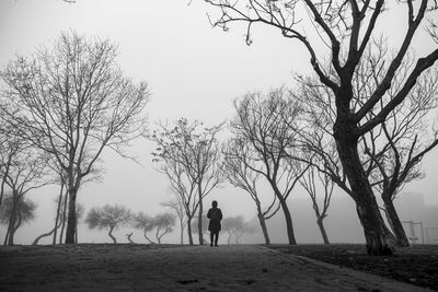 Silhouette man standing by bare trees on field against sky