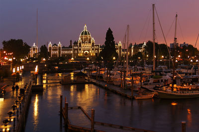 Boats moored in river with illuminated city in background