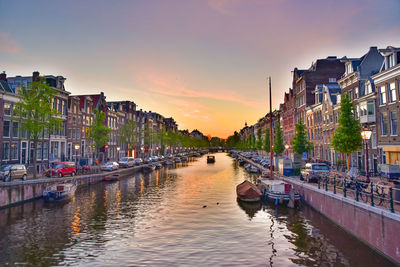 Boats moored in canal against buildings in city at sunset