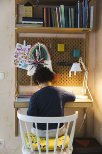 Rear view of boy sitting on chair by desk while studying at home