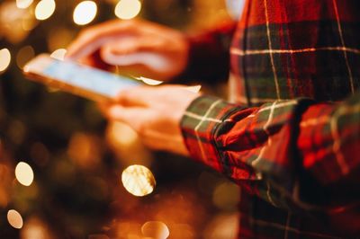 Midsection of man using smart phone against illuminated christmas tree