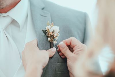 Cropped image of hands putting boutonniere on bridegroom suit