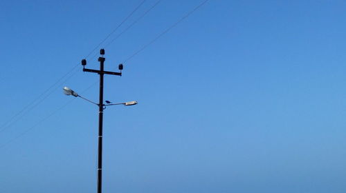 Low angle view of electricity pylon against clear blue sky
