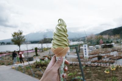 Close-up of hand holding ice cream against sky