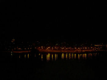 Illuminated buildings by river against sky at night