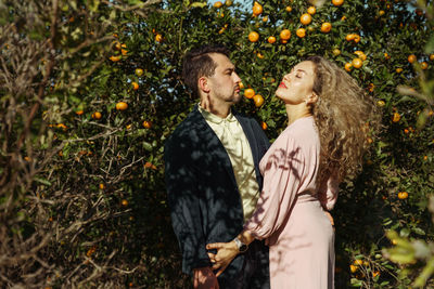 Portrait of young woman  and man standing against mandarin plants