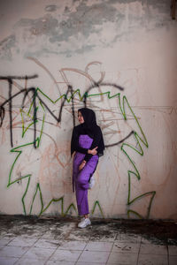 Full length of woman standing against graffiti wall