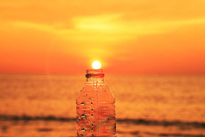 Illuminated bottle on beach against sky during sunset