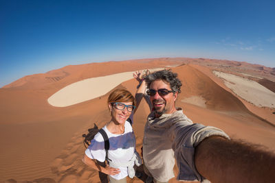 Portrait of smiling young woman standing on desert against clear sky