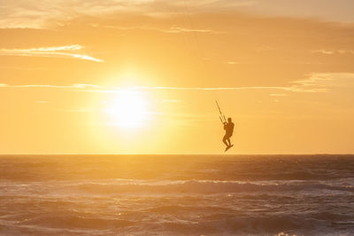 Man surfing in sea against sky during sunset