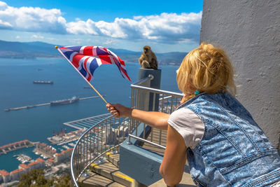 Woman holding flag while standing by railing against sky