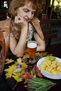 Senior woman with food and drink by autumn leaves on table sitting in cafe