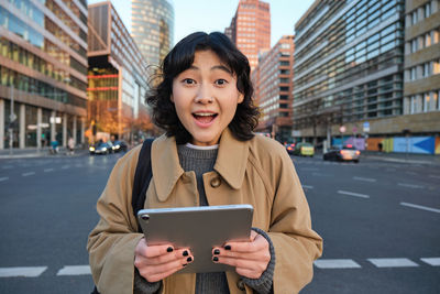 Portrait of young woman using digital tablet while standing in city