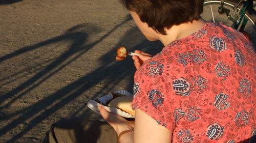 Woman having food while sitting on sidewalk