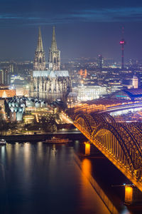 Illuminated bridge over river by buildings in city at night