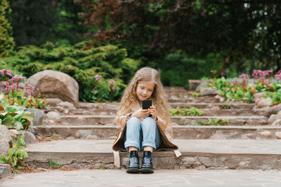 Seven year old girl communicates online on a smartphone, sitting in nature in the spring in the park