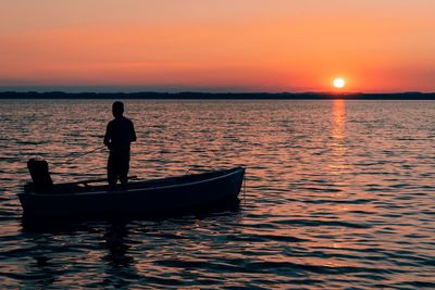 Silhouette man standing in sea against orange sky