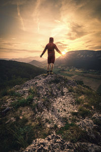 Rear view of man standing on land against sky during sunset