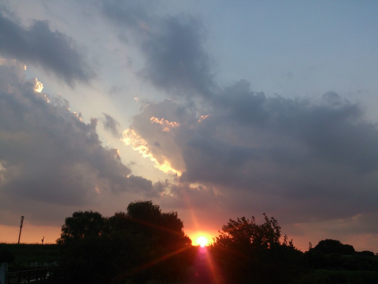 sunset, sun, silhouette, tree, sky, scenics, beauty in nature, tranquil scene, tranquility, cloud - sky, sunbeam, sunlight, nature, idyllic, orange color, low angle view, cloudy, cloud, lens flare, landscape