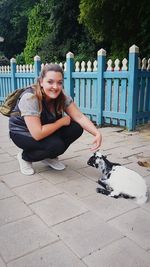 Portrait of woman crouching by kid goat relaxing on footpath