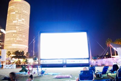 Crowd at illuminated city against clear blue sky at night