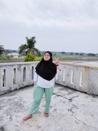 Full length portrait of young woman standing against sky