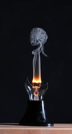 Close-up of smoke emitting from broken illuminated light bulb against black background