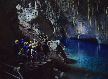 High angle view people standing by rock formation and sea in cave