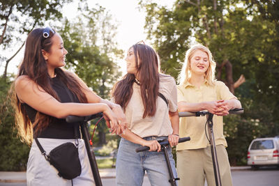 Young female friends spending time together outdoors riding electric scooters