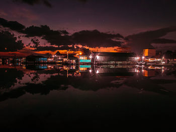 Illuminated buildings by lake against sky at night