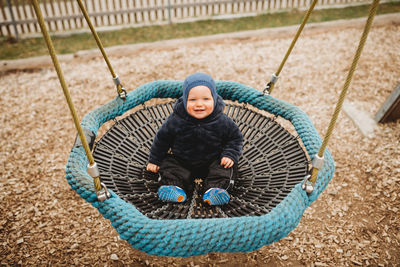Cute baby in outdoor playground in winter on a nest hammock