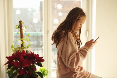 Young woman using phone while standing on window