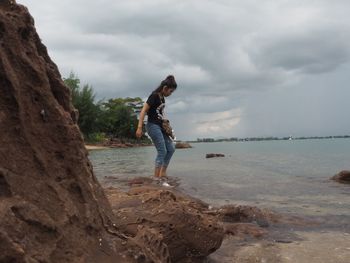 Side view of man on rock at beach against sky