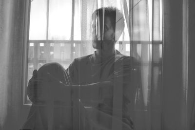 Man sitting by window seen through curtain