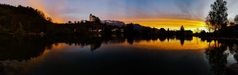 Scenic view of lake by buildings against sky during sunset